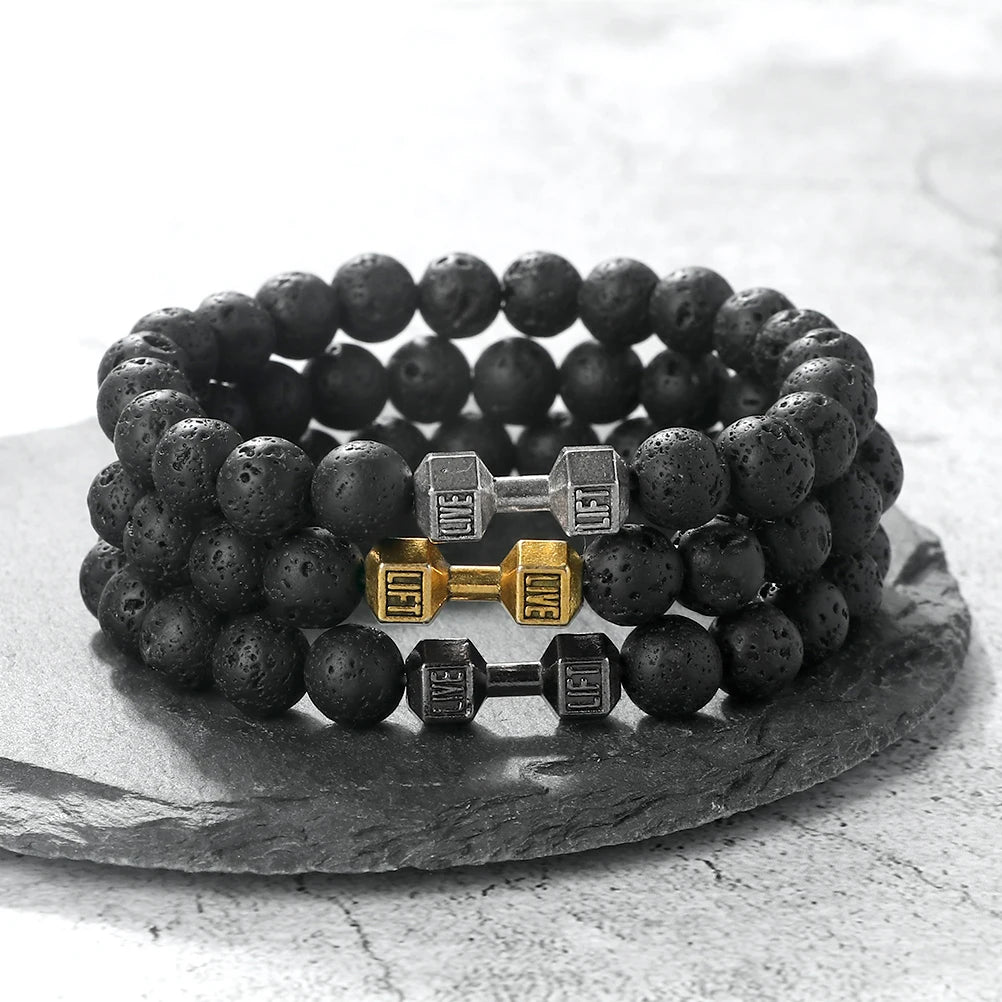 Black beaded bracelet with silver and gold dumbbell charms on a stone surface